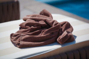 Brown towel draped over a poolside lounge chair with blue water in the background.