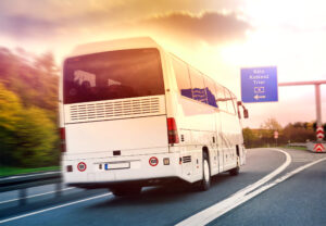 White tour bus driving on a curving highway at sunset, with a blue road sign reading Köln Koblenz Trier ahead.